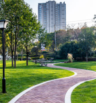 Commercial Interlocking Services Ajax Brick interlock pathway winding through a landscaped park area with benches, trees, and city buildings in view